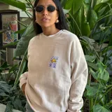 Buzo color beige de algodón y poliéster, con cuello redondo y puños acanalados. Presenta un pequeño estampado en el frente con una estrella de mar amarilla sobre un fondo a cuadros violeta y celeste.