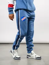 Pantalon de jogging azul de felpa, con franjas laterales en blanco y azul marino. Presenta el escudo del Club Nacional de Football en el muslo derecho y el logo de Umbro en el izquierdo.