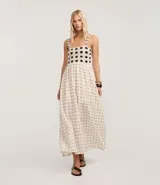 Vestido midi de algodón, color crema, con breteles finos. El corpiño presenta un diseño de crochet con motivos florales en azul marino, y la falda evasé tiene un estampado de pequeños íconos abstractos en azul.