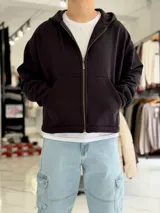 Campera tipo canguro con cierre frontal completa y capucha, de corte boxy fit en color blanco marfil. Presenta bolsillos frontales tipo parche y puños y dobladillo en rib elástico.