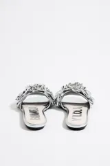 Sandalias plateadas con base plana y adorno de flores con volados en el empeine.