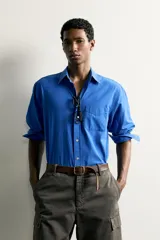 Camisa de corte relajado confeccionada en tejido de algodón de color azul, con cuello abotonado, manga larga, bolsillo frontal de parche y cierre de botones.
