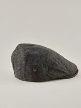 Boina estilo irlandés en color gris con textura jaspeada. Presenta un detalle lateral en cuero marrón con un botón metálico decorativo y visera integrada.