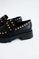 Mocasines de cuero color marrón con suela track negra y tachas doradas.