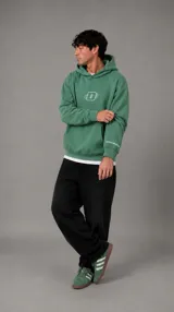 Hoodie de algodón color verde, con capucha, bolsillo frontal tipo canguro y logo bordado en el pecho. Presenta detalles de marca en la manga y puños acanalados.