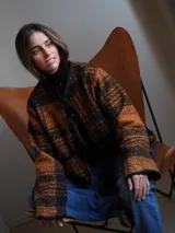 Chaqueta corta con estampado a cuadros en tonos negro, gris y marrón, con ribetes en marrón y cierre frontal con lazos.