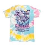 Remera de algodón con estampado gráfico de Alf relajándose en una playa, sobre un fondo con efecto batik en tonos amarillo, celeste y rosado.