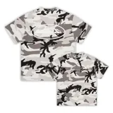 Camiseta de corte regular con estampado de camuflaje en tonos grises y blancos. Presenta un logo ovalado blanco con una imagen en el centro.