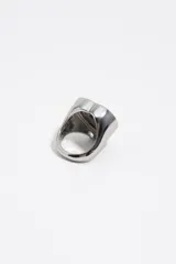 Anillo de metal plateado con diseño de corazón. Presenta un centro esmaltado en color rosado y un borde con letras de colores y detalles grabados.