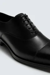 Zapato de vestir tipo Oxford en color negro, con diseño de puntera reforzada y cierre mediante cordones. Presenta una silueta clásica y elegante con tacón bajo.