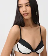 Top de bikini Bossa Nossa con diseño color block en negro y blanco, confeccionado en microfibra con textura plisada. Presenta copa estructurada con aro, breteles finos regulables y un detalle de botón decorativo en el centro.