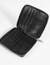 Billetera pequeña de cuero vegano color lila claro, con cierre perimetral de cremallera y tirador metálico. Presenta un logo metálico en bajo relieve en el frente.