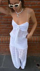 Pollera larga de encaje blanco con volados en el ruedo. Tiene un top a juego con breteles finos y volados en el busto, con un lazo en el centro.