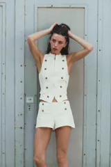 Short mini de tiro bajo color blanco con aplicación de botones dorados frontales y cierre lateral con cremallera oculta.