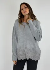 Sweater gris de tejido de punto con cuello redondo y mangas largas. Presenta un aplique de círculos concéntricos en el ruedo.