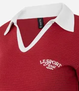 Blusa tipo polo de manga corta, color rojo, con cuello y escote en V con bies blanco contrastante. Presenta una textura gofrada y un bordado pequeño en el pecho con el texto "LE SPORT Paris".