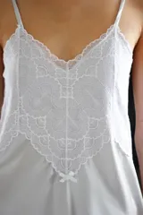 Camisón corto de satén color crema con detalles de puntilla gris en el escote y en el ruedo. Presenta breteles finos ajustables y un diseño fluido.