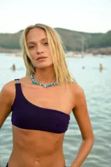Bikini de tela lúrex color violeta con acabado brillante. El corpiño es tipo top de un solo hombro con hebilla metálica decorativa en el tirante. La bombacha es de corte vedetina.