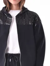 Campera deportiva negra con capucha, cierre frontal y apliques de lentejuelas en los hombros.