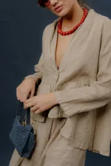 Chaqueta de lino color beige, de calce relajado, con escote en V, cierre frontal con botones y bolsillos frontales aplicados.