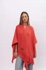 Ruana de tejido de punto color coral con flecos en el ruedo y etiqueta de cuero con logo grabado en la parte frontal.