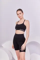 Top deportivo negro con breteles finos y elástico inferior con la marca Bassi estampada en gris. Diseño de espalda cruzada que brinda soporte y sujeción.