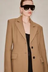Abrigo largo entallado de Zara Woman Collection, confeccionado en mezcla de lana color tostado. Presenta cuello con solapa de muesca, mangas largas, bolsillos con solapa en el frente, forro interior y cierre frontal de dos botones oscuros.