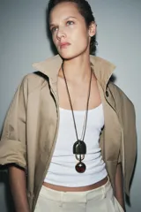 Pack de dos collares. Uno con cordón negro y colgante ovalado de resina marrón y metal dorado. El otro con cordón metálico dorado y colgante de pieza metálica con aplicación de piel verde. Ambos con cierre de bola ajustable.