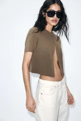 Chaqueta corta color verde oliva, de tejido de punto con cuello redondo y manga corta. Cierre frontal con un único botón dorado.