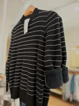 Sweater de punto negro con rayas horizontales blancas finas, cuello medio alto y mangas largas. Presenta un diseño ajustado al cuerpo con interior afelpado para mayor abrigo.