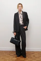 Blazer de corte sastrero en color gris oscuro, con cierre frontal de un botón, solapas clásicas y bolsillos con solapa. Presenta una estructura entallada y hombreras marcadas.