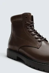 Bota tipo derby con cordones, confeccionada en material liso con horma redonda y suela track con volumen.