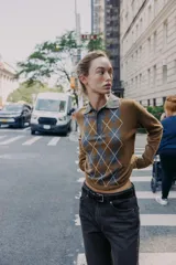 Jersey de punto con cuello polo y cierre frontal de botones. Presenta un diseño de estampado de rombos en el frente en tonos gris y blanco sobre una base color marrón.