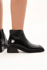Bota corta de cuero negro con acabado brillante, diseño de punta cuadrada y taco bloque. Presenta cierre lateral interno y detalle de ribete en la capellada.