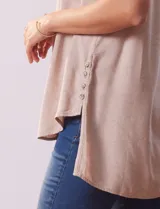 Camisa sin mangas color beige, marca Zac & Rachel, confeccionada en lino. Presenta escote en V, abertura frontal con botones, dos bolsillos delanteros y terminación con botones en los laterales.