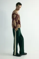 Pantalón deportivo de corte relajado en tejido efecto neopreno, color verde oscuro con franjas laterales en contraste color crema. Presenta cintura elástica con cordón ajustable, bolsillos laterales y traseros, y cierre oculto en el bajo.