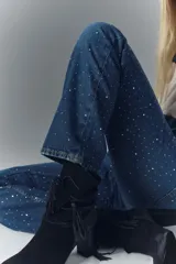 Jean tiro alto de denim azul rígido, con lavado oscuro y apliques de brillos. De pierna recta.