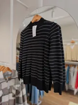 Sweater de punto negro con rayas horizontales blancas finas, cuello medio alto y mangas largas. Presenta un diseño ajustado al cuerpo con interior afelpado para mayor abrigo.