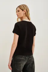 Remera negra de algodón con cuello redondo y manga corta. Presenta un aplique bordado en el pecho con forma de corazón rojo que contiene un ojo detallado con mostacillas y bordados.