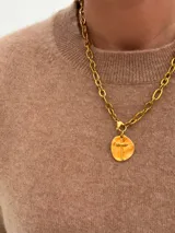 Collar de cadena de eslabones gruesos con baño de oro, que presenta un dije circular con una cruz en relieve.