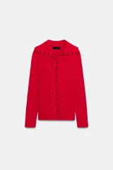 Chaqueta de punto color rojo, con cuello solapa y manga larga. Cierre frontal con fila de botones negros en contraste que se extienden también sobre el cuello.