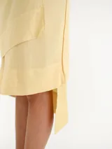 Pollera midi color amarillo claro, tipo envolvente (wrap), con diseño asimétrico en capas y lazo lateral para anudar.