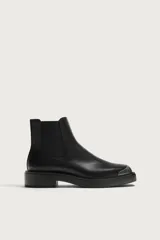 Botas Chelsea de cuero negro con paneles elásticos laterales, suela gruesa y puntera redonda reforzada con una pieza metálica plateada.