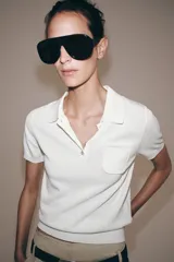 Top negro de punto fino con cuello polo, manga corta, cierre frontal de botones y un bolsillo de parche en el pecho.