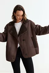 Chaqueta de estilo aviador en color marrón, confeccionada en material simil gamuza con interior y solapas de corderito sintético. Presenta cierre frontal con botones, corte holgado y mangas largas.