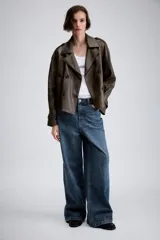 Cazadora de Zara Woman Collection confeccionada en material efecto piel color marrón oscuro. Presenta cuello con solapas, cierre frontal cruzado con botones, bolsillos delanteros y mangas largas con trabillas y hebillas ajustables en los puños.