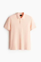 Remera polo color salmón de piqué de algodón, corte regular fit, con cuello clásico, tapeta de dos botones, mangas cortas y terminaciones acanaladas en cuello y mangas.