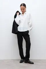 Camisa blanca de manga larga con puños abotonados y fruncidos, hombros fruncidos y cierre frontal con botones.