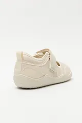 Zapatilla tipo guillermina de estilo barefoot, color beige con detalles en rosa pálido en el talón y tira de ajuste con velcro. Posee suela plana y flexible diseñada para un movimiento natural del pie.