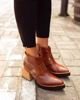 Botineta de cuero negro con diseño combinado en cuero charolado, plataforma y taco cuadrado de madera clara. Presenta cierre lateral y puntera redondeada.